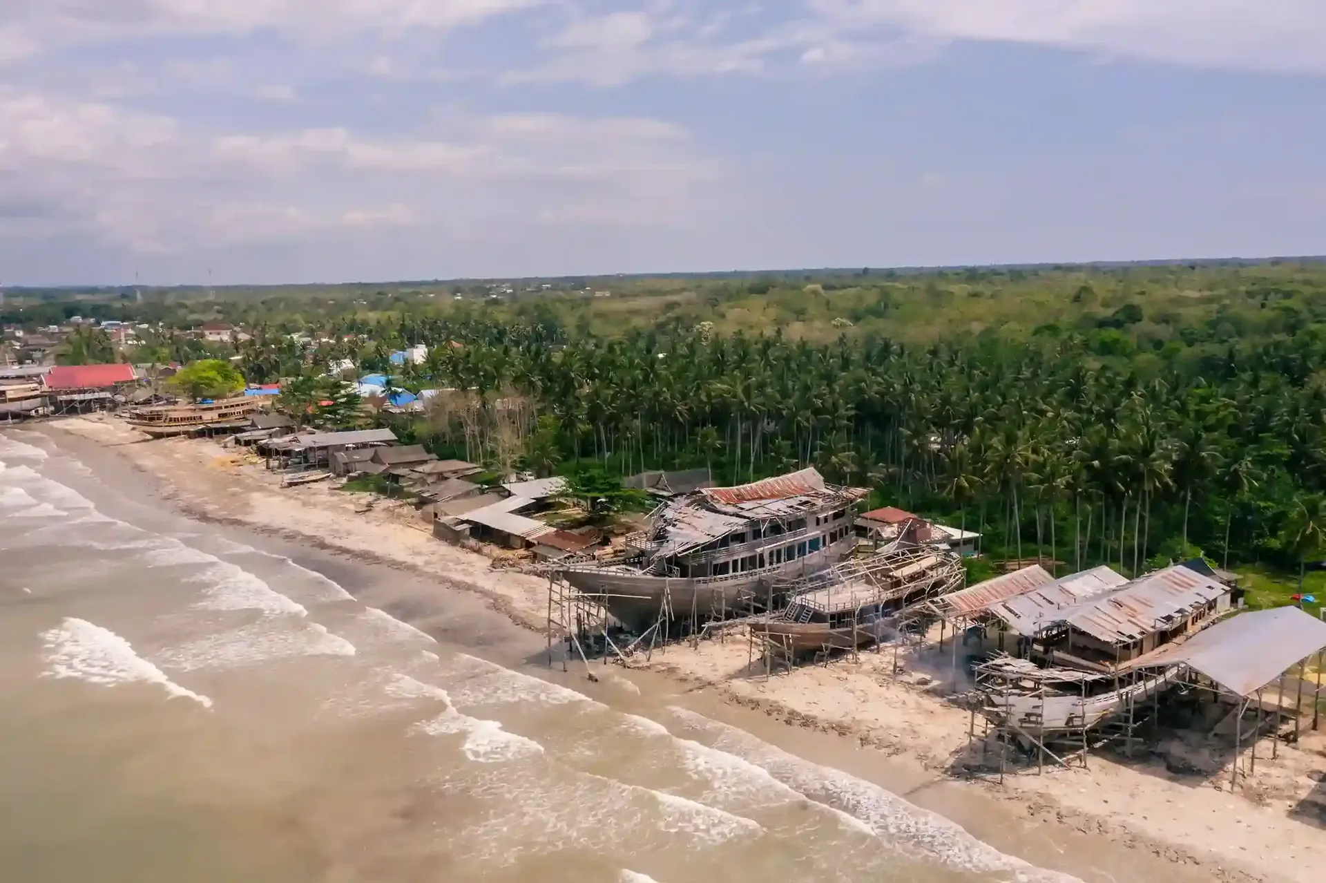 Aerial view of a beach boatyard with wooden hulls under construction